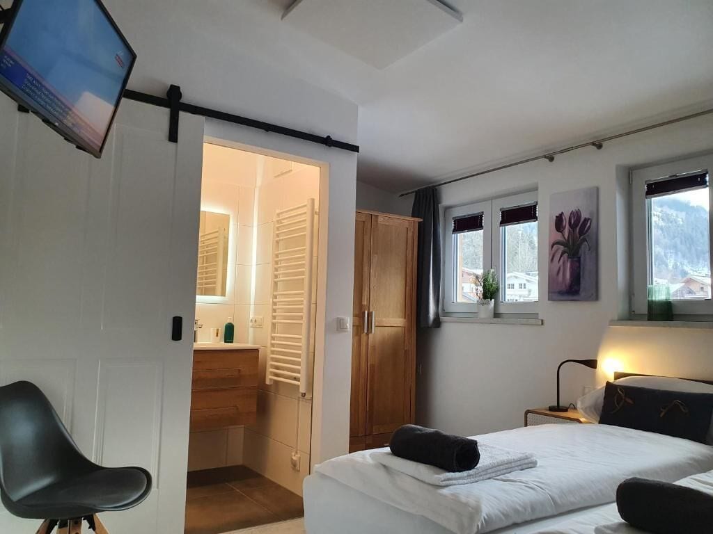 Ein Schlafzimmer mit Bett, Schreibtisch, Stuhl, Kleiderschrank, Fenster mit Aussicht und einem Flachbildfernseher.
