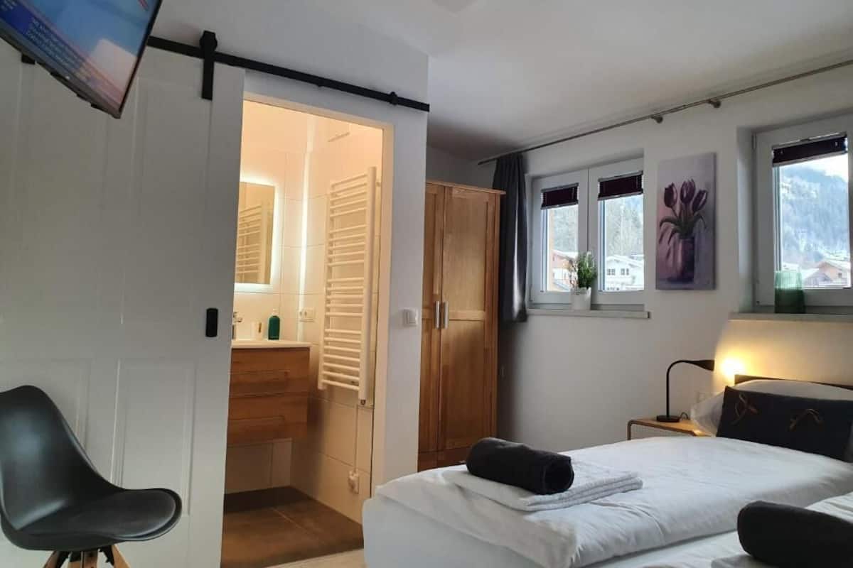 Ein Schlafzimmer mit Bett, Schreibtisch, Stuhl, Kleiderschrank, Fenster mit Aussicht und einem Flachbildfernseher.