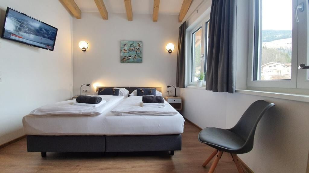 Ein Schlafzimmer mit einem Bett, Nachttischen, einem Sessel, einem Fernseher und einem Gemälde.