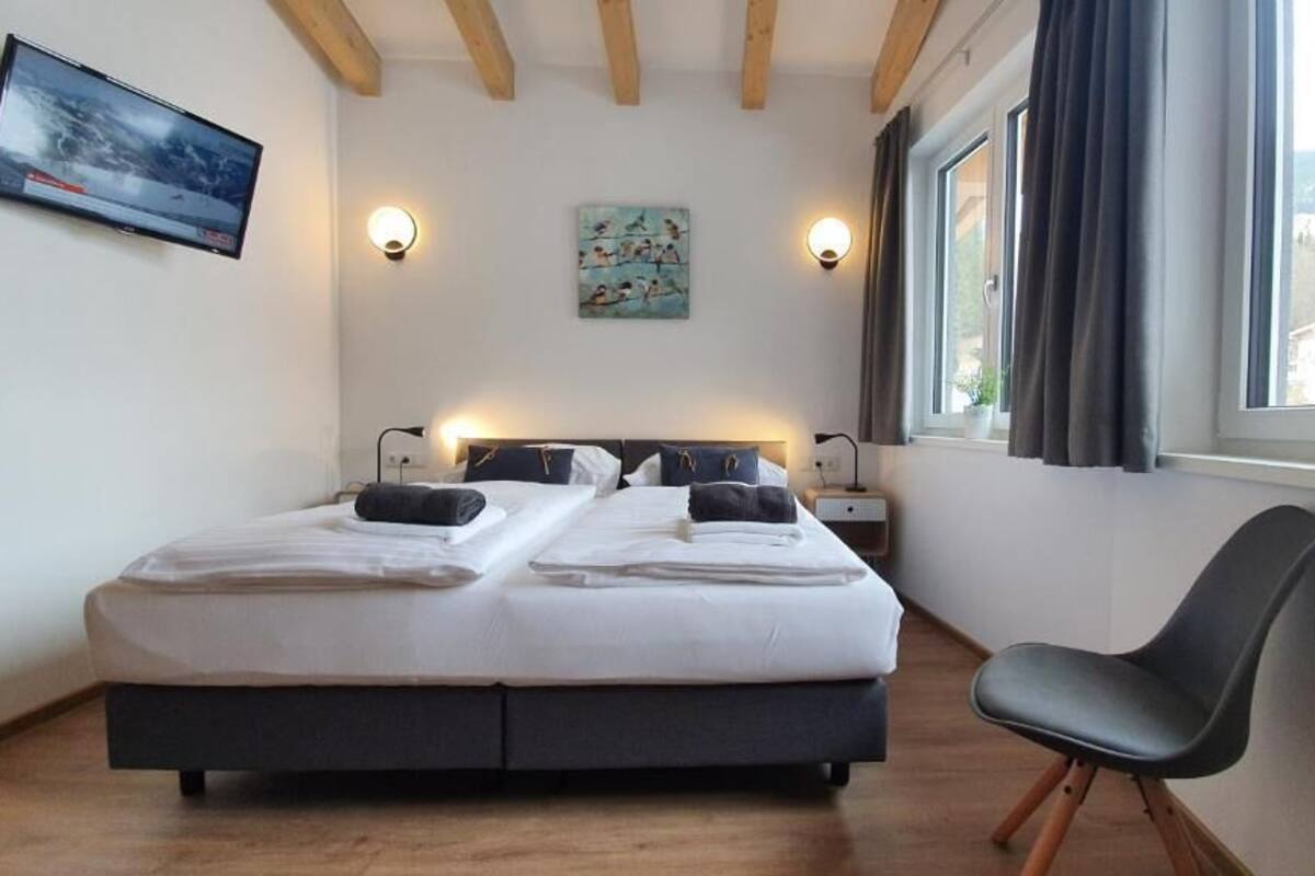 Ein Schlafzimmer mit einem Bett, Nachttischen, einem Sessel, einem Fernseher und einem Gemälde.