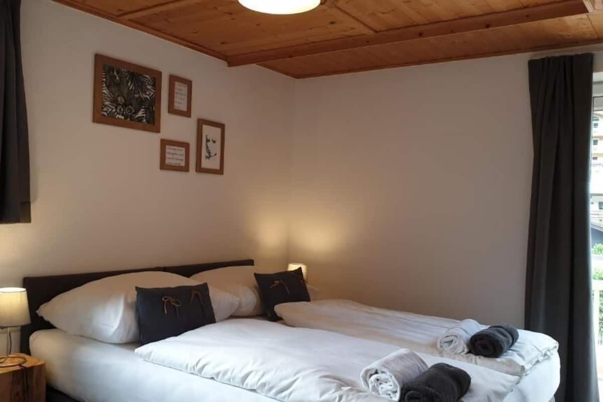 Ein Schlafzimmer mit Bett, Kissen, einem Nachttisch und gerahmten Bildern an der Wand.