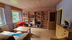 A room with a wooden ceiling, a bookshelf, a desk, a chair, and a window.