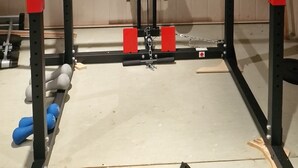 Een fitnessruimte met een squat rek, een stang en gewichtsschijven.