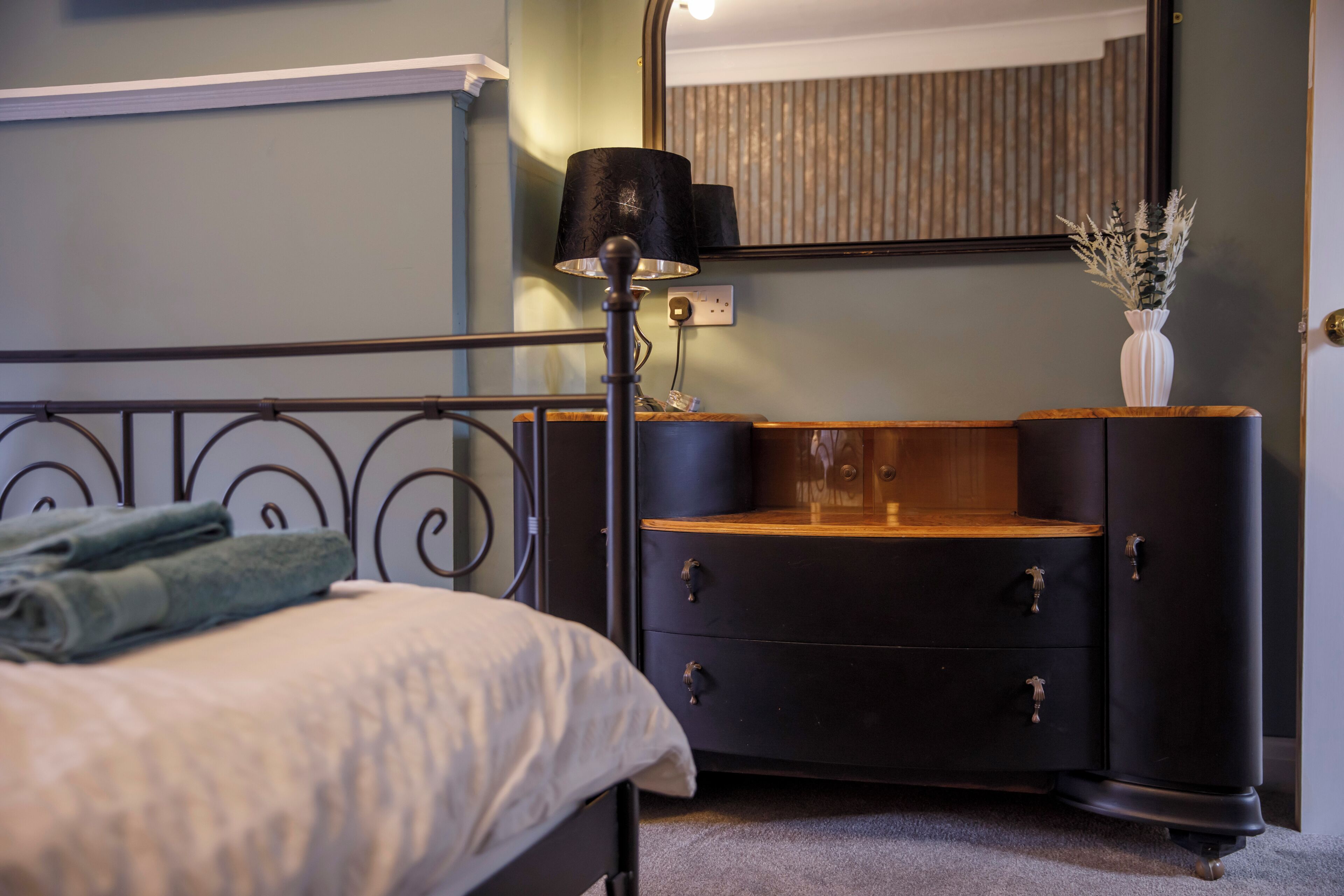 A bedroom with a bed, a dresser, a mirror, and a lamp.