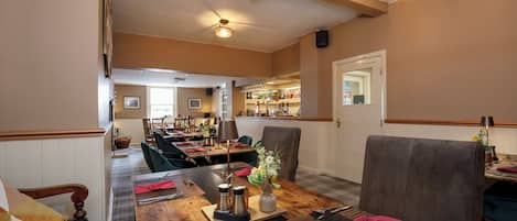 Un restaurante con mesas y sillas de madera, y una zona de bar.