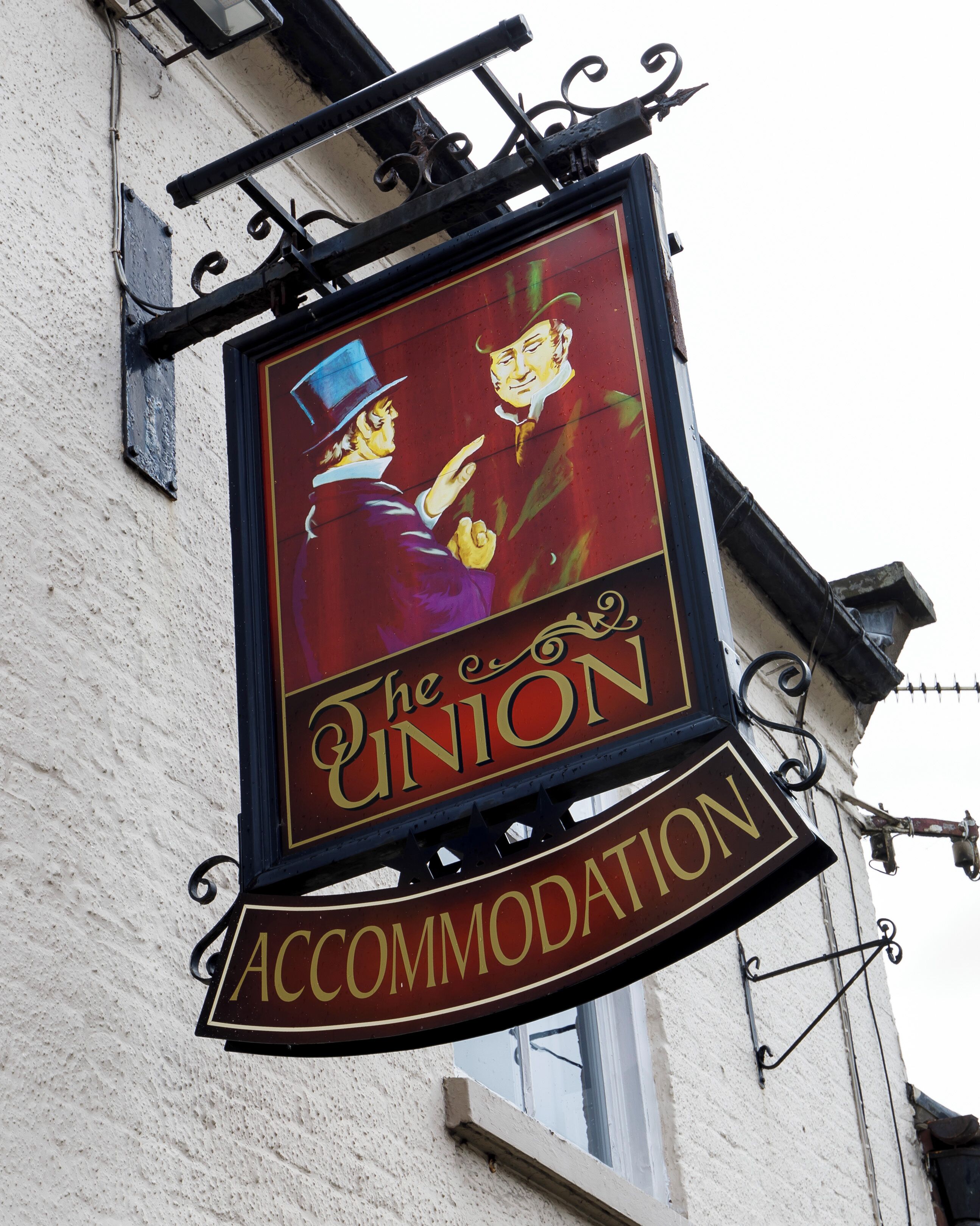 Señal para 'The Union Accommodation' con un diseño vintage, montada en un edificio de pared blanca y herrajes de metal negro.