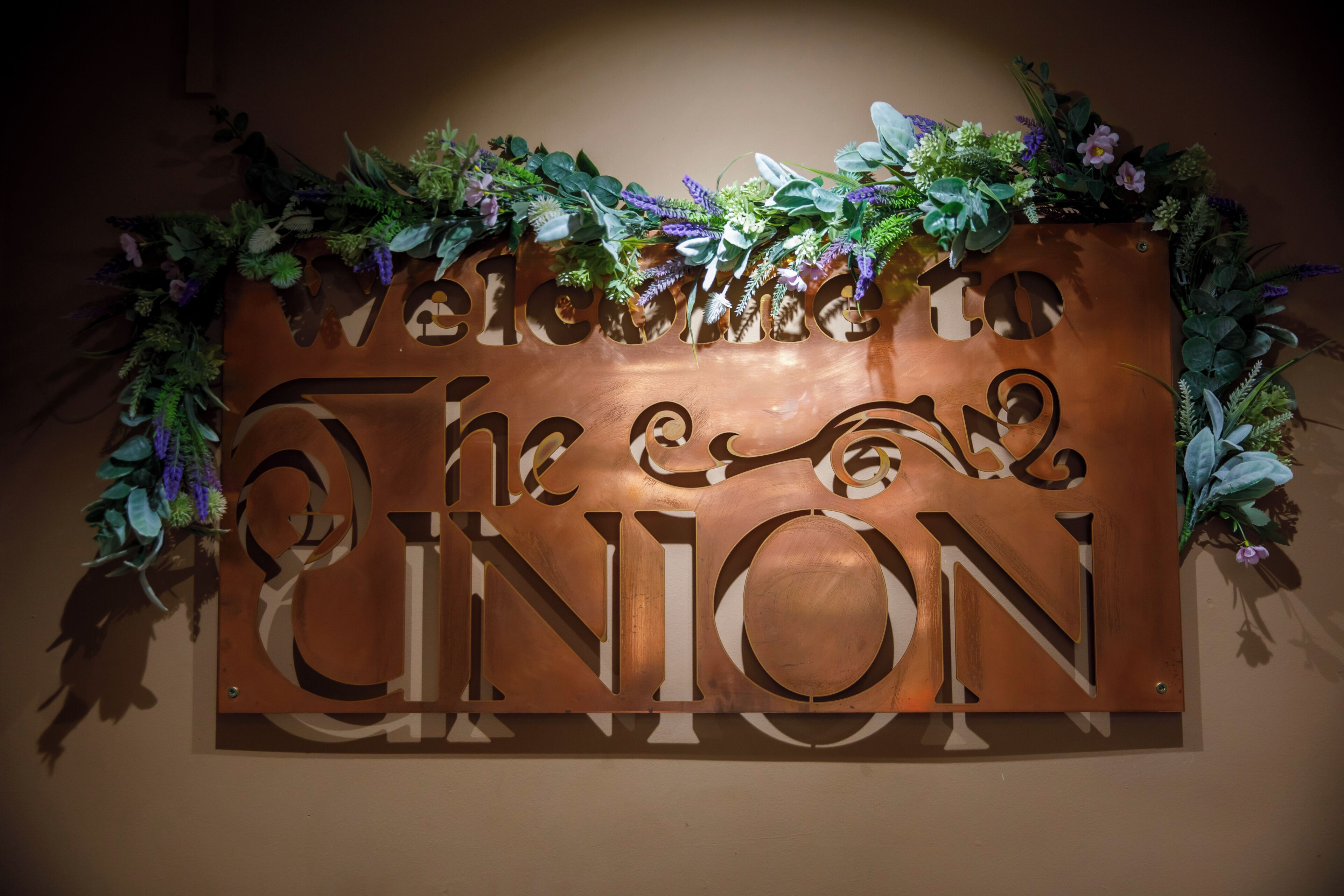 Un letrero de bienvenida con la inscripción 'Welcome to The Union' en letras grandes, rodeado de follaje decorativo.
