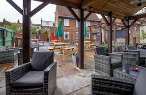 An outdoor patio with wicker furniture, stone flooring, and brick buildings in the background.