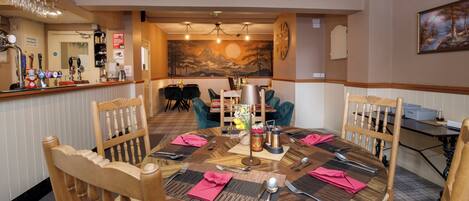 A dining area with a round table set for four, wooden chairs, a bar with multiple taps, and a mural on the wall.