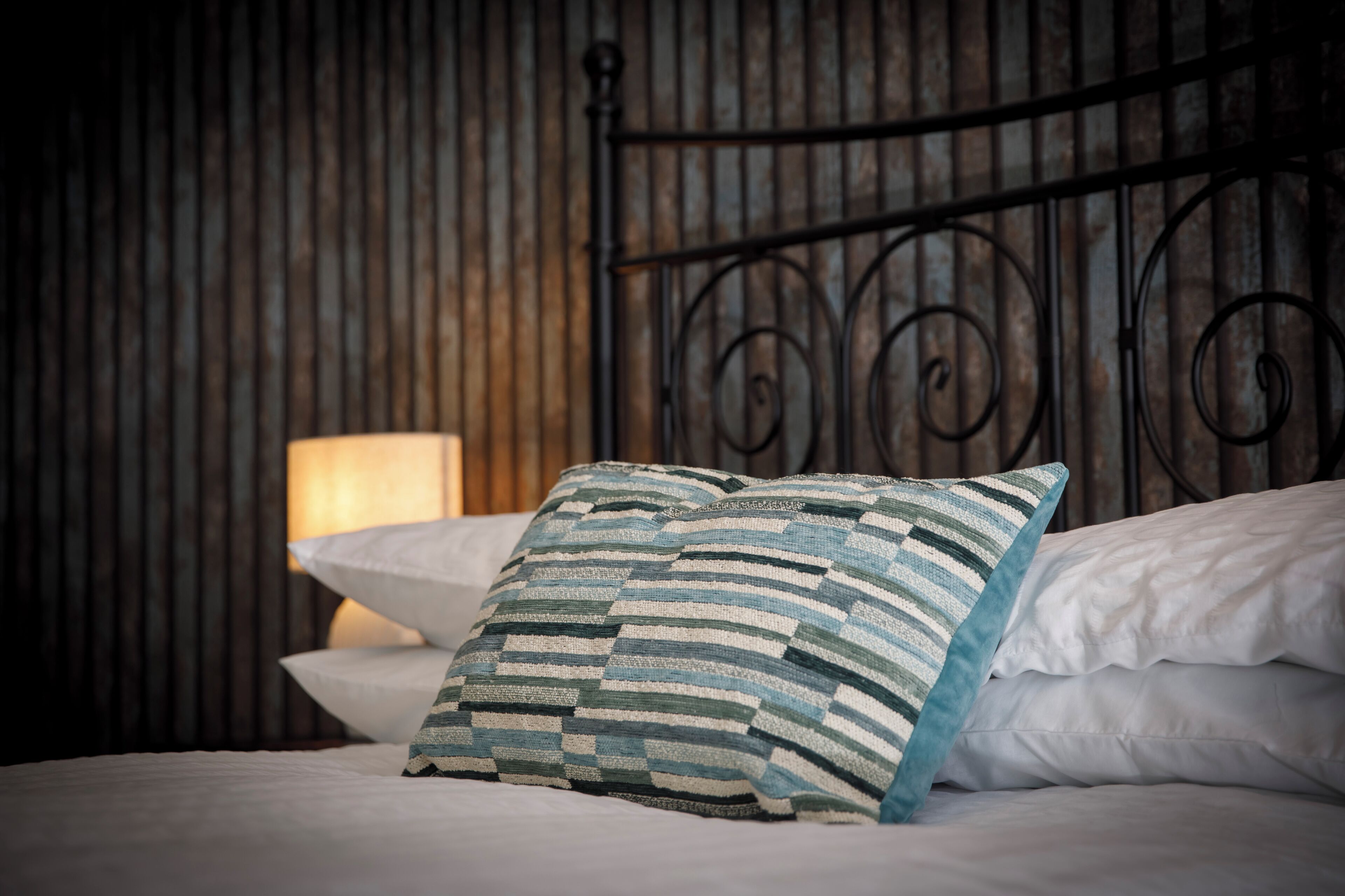 A bed with a striped pillow, a plain pillow, and a metal headboard.