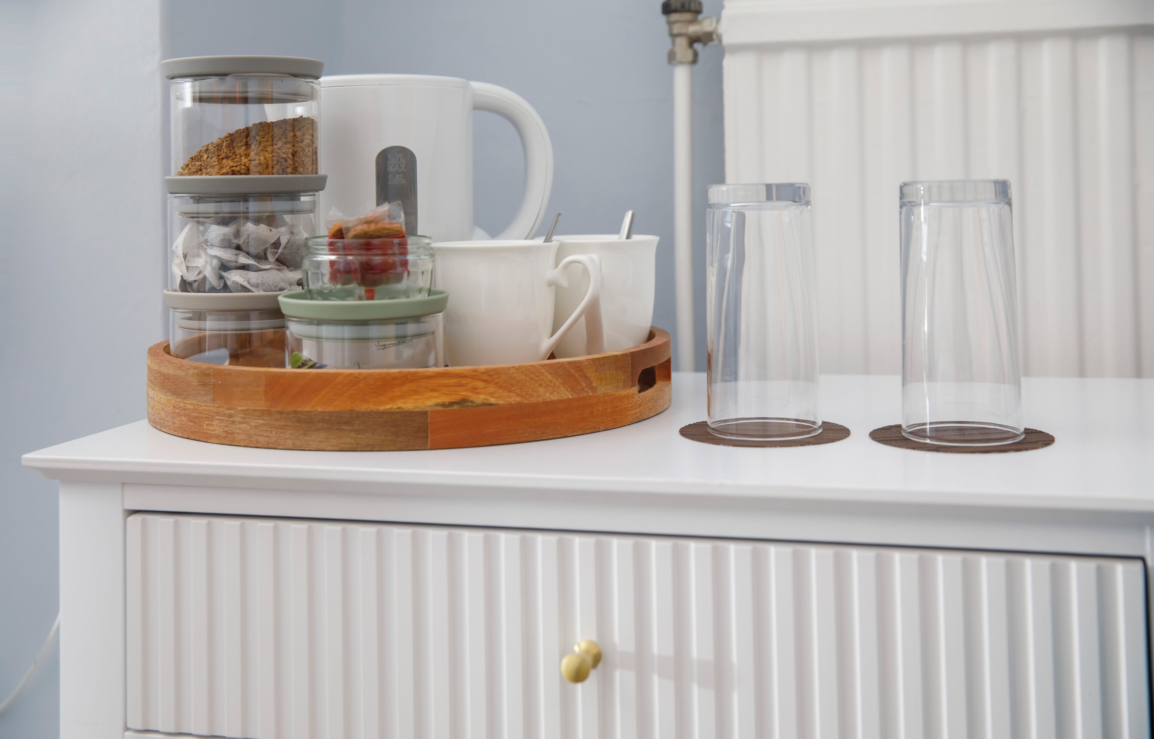 A white cabinet with a tray holding jars, a mug, and a glass.