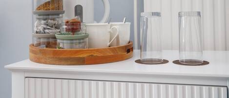 A white cabinet with a tray holding jars, a mug, and a glass.