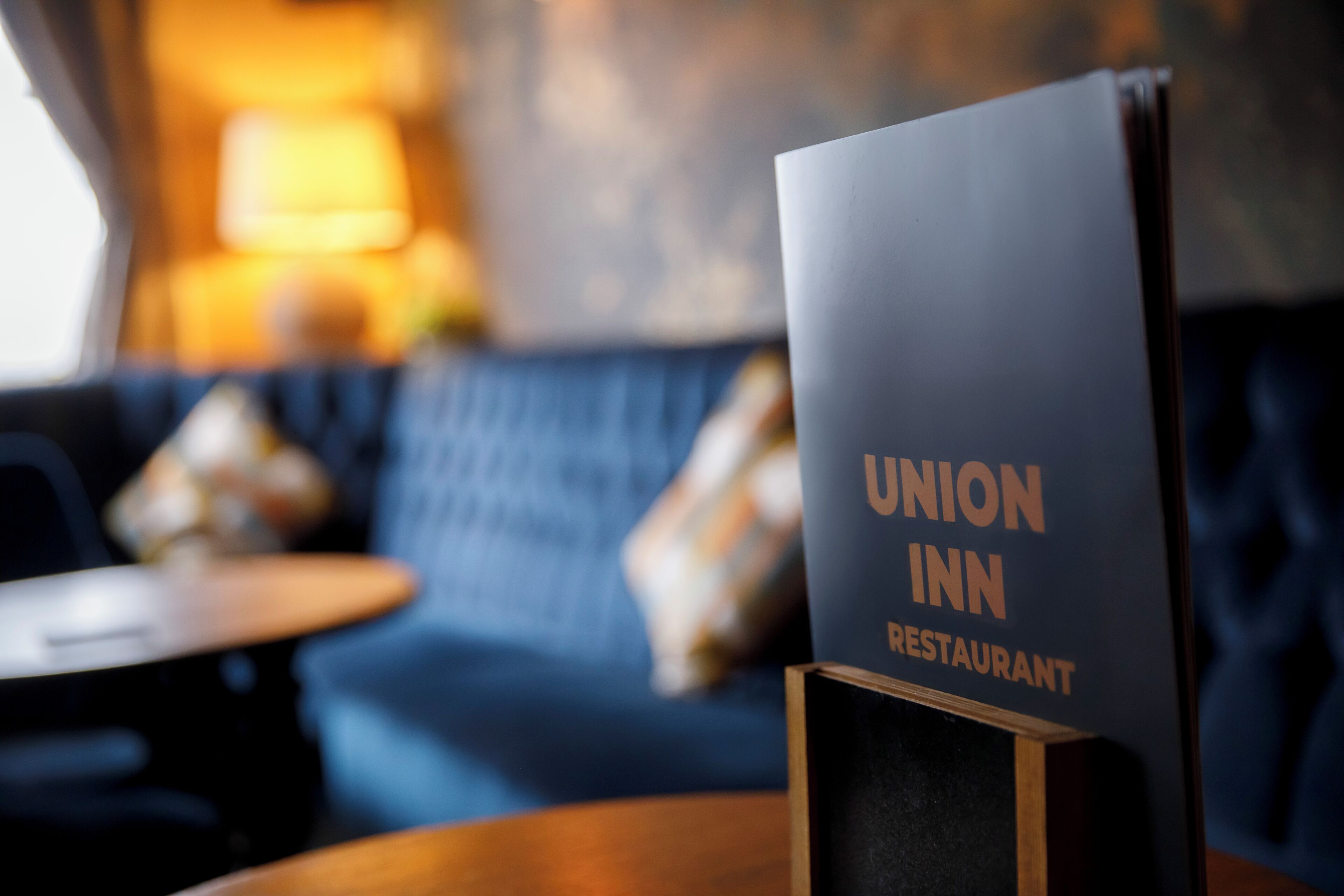 A menu stand for Union Inn Restaurant with a blurred background of a blue sofa and a small round table.