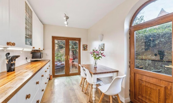 Une cuisine avec des meubles de rangement en bois, une table à manger avec des chaises, un four encastré et une grande fenêtre.