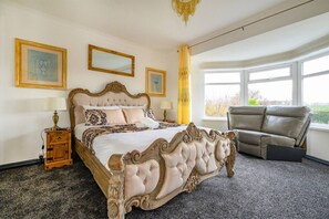 A bedroom with a large bed, a nightstand, a chair, and a window with a view. - CH-Stylish Home with Hot Tub & Garden (West Yorkshire)