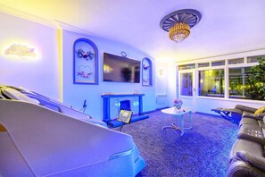 A room with a fireplace, a television, a chandelier, and a window with a view. - CH-Stylish Home with Hot Tub & Garden (West Yorkshire)