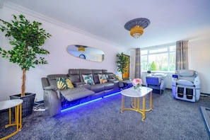 Ein modernes Wohnzimmer mit einer Couch, einem Massagesessel und einem kleinen Tisch mit einer Blumenvase.