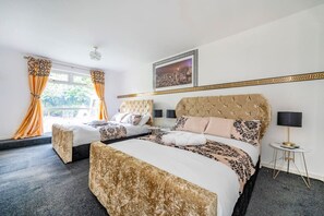 Ett hotellrum med två sängar, ett stort fönster med gardiner, en inramad tavla på väggen och ett litet nattduksbord med en lampa.