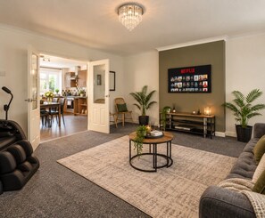 Een woonkamer met een open haard, een salontafel en een bank. Achtergrond toont een eethoek.