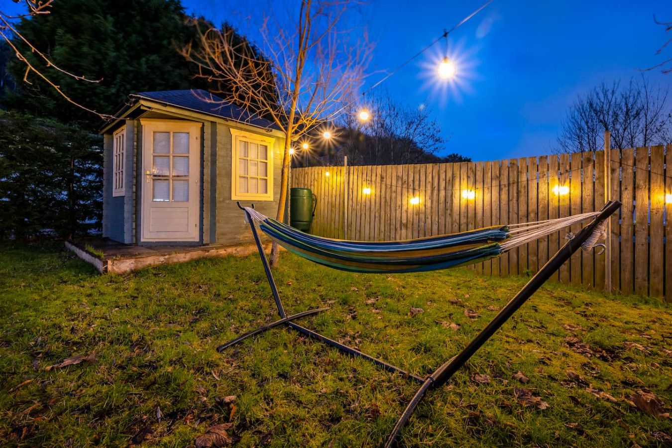 Un hamac dans un jardin, avec une clôture en bois et un petit abri de jardin.