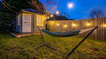 A hammock in a backyard with a wooden fence and a small shed.
