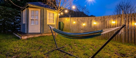 A hammock in a backyard with a wooden fence and a small shed.