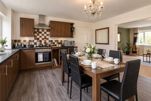 A modern kitchen with wooden cabinets, a dining area with a table set for six, and a chandelier. - Cozy Farm house with Hot Tub retreat (West Yorkshire)