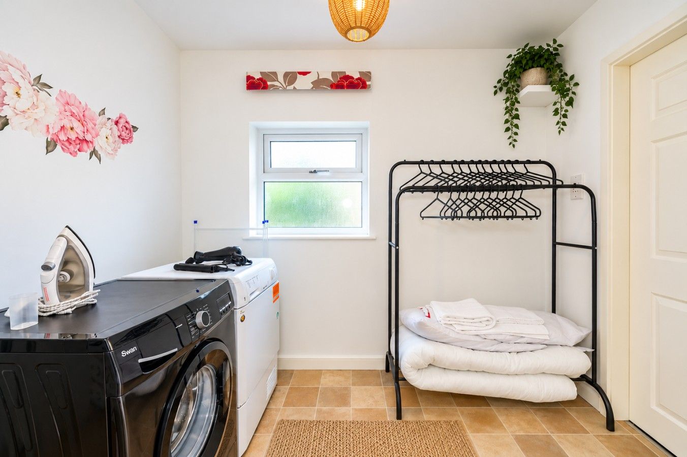 A laundry room with a washing machine, an iron, a drying rack, and a window.