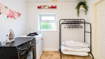 A laundry room with a washing machine, an iron, a drying rack, and a window.
