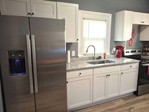 Una cocina moderna con gabinetes blancos, electrodomésticos de acero inoxidable, encimera de granito y una ventana con persianas.