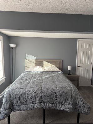 Un dormitorio con cama, mesita de noche, lámpara y una puerta.