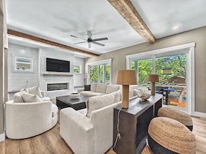 A modern living room with a fireplace, a ceiling fan, and a view of the outdoors. - Spacious 7BR home with pool, free golf cart, fenced yard & near beach (Hilton Head Island)