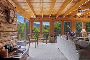 Interior de una cabaña de troncos con techo de madera, un sofá, sillas, una mesa y un reloj.
