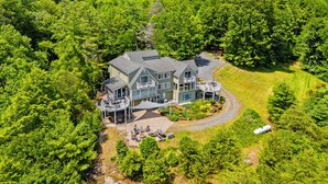 A large house surrounded by dense forest, with a driveway leading to a guest area.