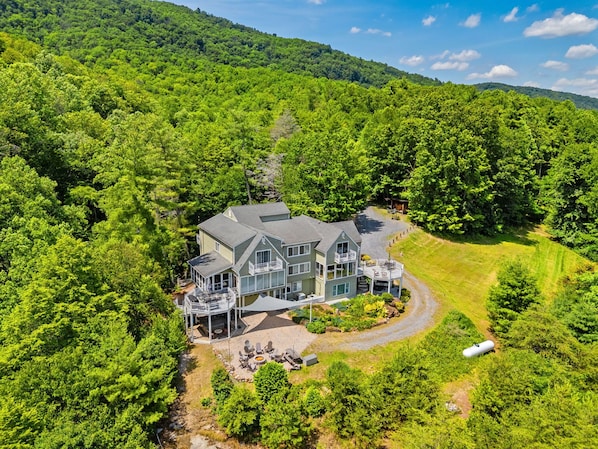 A large house surrounded by dense forest, with a driveway leading to a guest area.