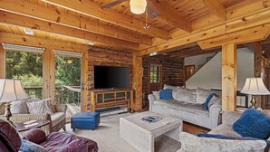A log cabin interior with a TV, sofas, and a staircase.