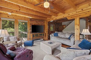 A log cabin interior with a TV, sofas, and a staircase.
