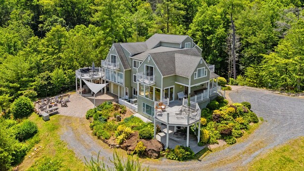 A large, two-story house with multiple balconies, surrounded by dense forest.