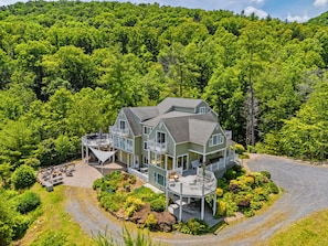 A large, two-story house with multiple balconies, surrounded by dense forest.