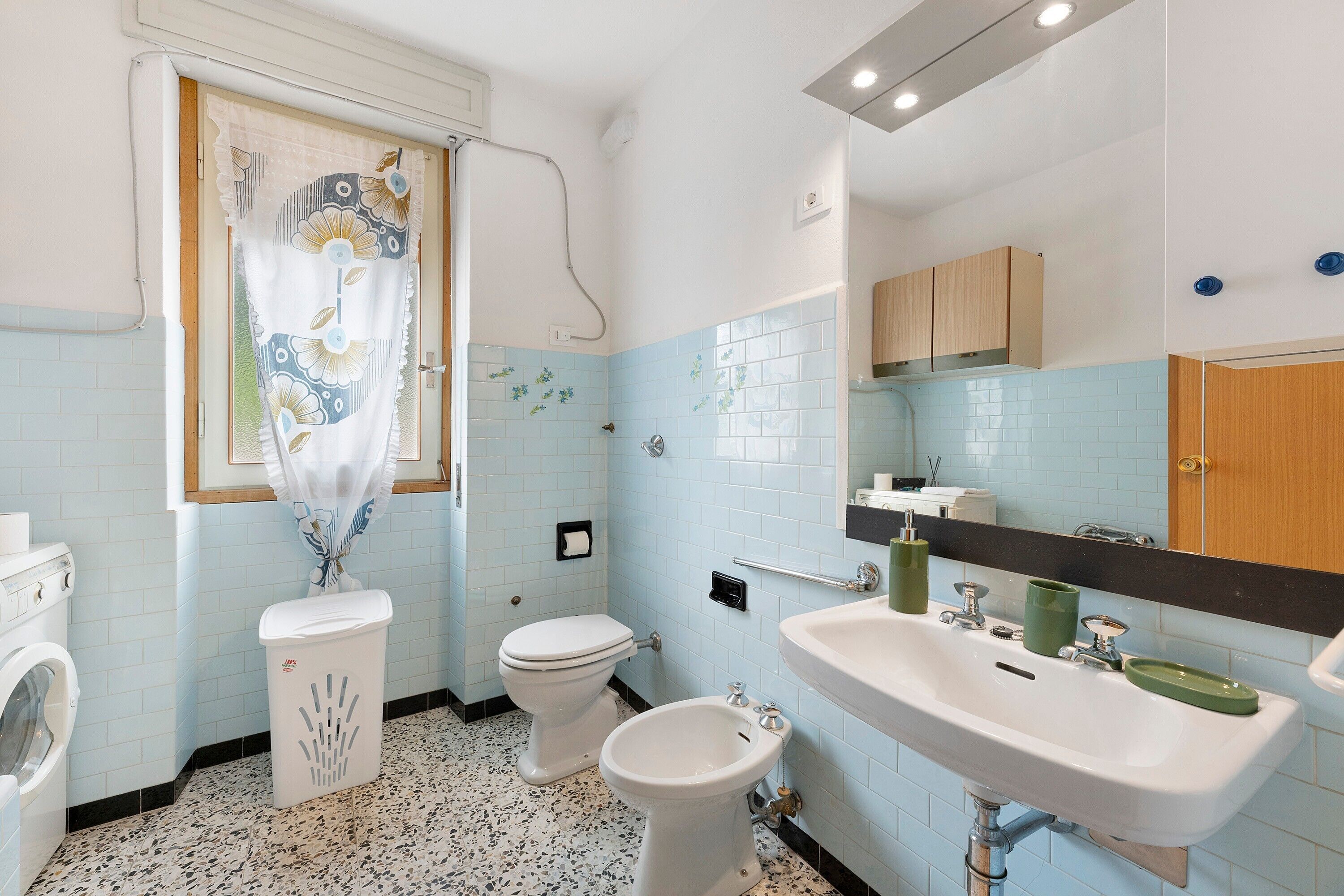 Ein Badezimmer mit Toilette, Bidet, Waschmaschine, Waschbecken und gefliesten Wänden.