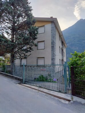A multi-story building with a stone facade, a gated entrance, and a mountain backdrop.
