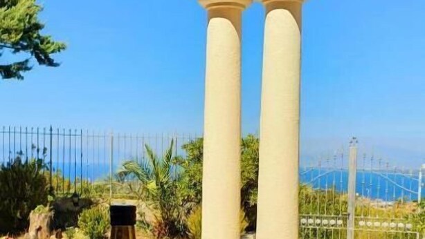 A table with a bottle of Cucinaiello olive oil and a bowl of salad, set against a clear blue sky with a view of the sea and a bridge. - Domus Mare Cilento (Agropoli)