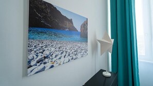 A wall-mounted painting of a rocky beach with a sailboat, a white star-shaped light fixture, and teal curtains. - Domus Mare Cilento (Agropoli)