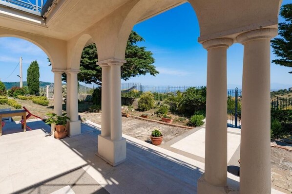 A covered outdoor area with columns, potted plants, and a view of the landscape.