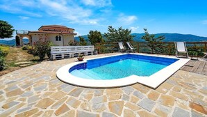 A swimming pool with stone flooring, a wooden deck, and a view of the mountains. - Domus Mare Cilento (Agropoli)