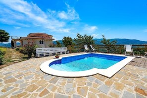 Una piscina amb paviment de pedra, un solàrium de fusta i vista a les muntanyes.