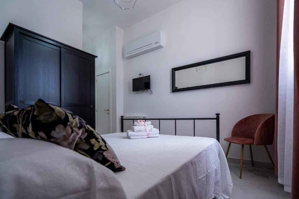 Un dormitorio con cama, armario, televisor, un cuadro enmarcado y una silla.