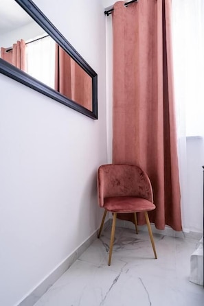 A corner room with a chair, a mirror, and a window with curtains.