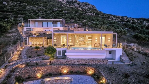 Uma casa moderna de dois andares com piscina, caminhos de pedra e montanhas ao fundo.