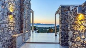 Corredor de paredes de pedra que leva a um terraço com vista para a paisagem e montanhas ao longe.